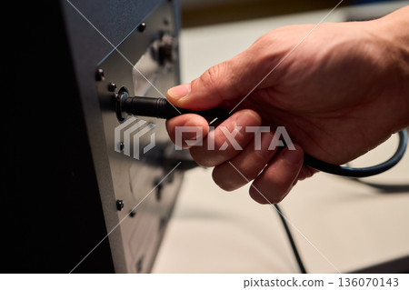 Setting up audio connection professionally, Attaching sound cable to subwoofer in studio, Closeup of hands securing audio cable into subwoofer in recording studio setting Setting up audio connection professionally, Attaching sound cable to subwoofer in studio, Closeup of hands securing audio cable into subwoofer in recording studio setting 136070143