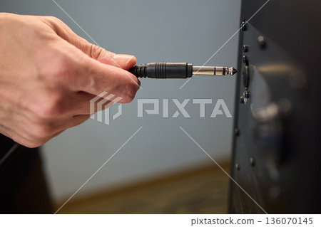 Setting up audio connection professionally, Attaching sound cable to subwoofer in studio, Closeup of hands securing audio cable into subwoofer in recording studio setting Setting up audio connection professionally, Attaching sound cable to subwoofer in studio, Closeup of hands securing audio cable into subwoofer in recording studio setting 136070145