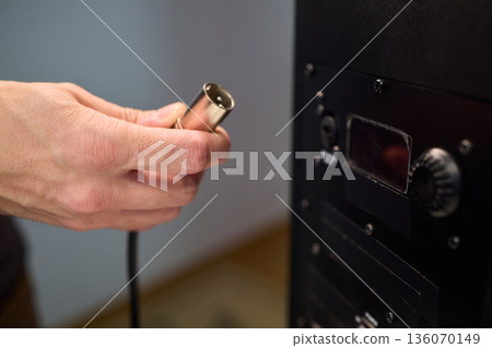 Setting up audio connection professionally, Attaching sound cable to subwoofer in studio, Closeup of hands securing audio cable into subwoofer in recording studio setting 136070149