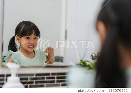 girl child brushing teeth at reflection in mirror in bathroom 136070331