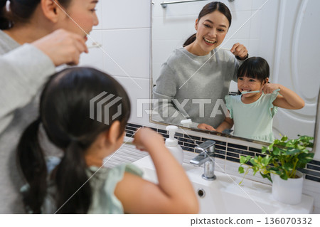 mother teaching girl child to brushing teeth at reflection in mirror in bathroom mother teaching girl child to brushing teeth at reflection in mirror in bathroom 136070332