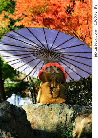 Jizo statue standing with a spectacular view of autumn leaves behind 136070498