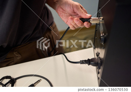 Setting up audio connection professionally, Attaching sound cable to subwoofer in studio, Closeup of hands securing audio cable into subwoofer in recording studio setting 136070530