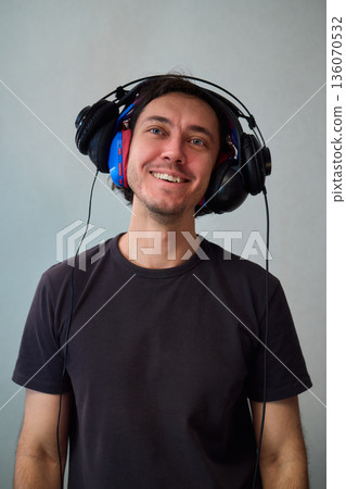 Happy guy with headphones, Casual man showcases vibrant headphones, Casually dressed man with curly hair showcases playful headphones during informal indoor photography session Happy guy with headphones, Casual man showcases vibrant headphones, Casually dressed man with curly hair showcases playful headphones during informal indoor photography session 136070532