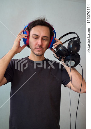 Happy guy with headphones, Casual man showcases vibrant headphones, Casually dressed man with curly hair showcases playful headphones during informal indoor photography session 136070534