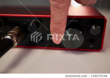 Adjusting audio controls, Precise handling of control knobs on audio equipment during setup, Fingers align control dials on audio interface for optimal sound calibration Adjusting audio controls, Precise handling of control knobs on audio equipment during setup, Fingers align control dials on audio interface for optimal sound calibration 136070546
