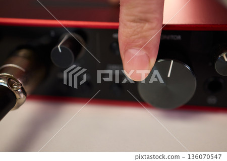 Adjusting audio controls, Precise handling of control knobs on audio equipment during setup, Fingers align control dials on audio interface for optimal sound calibration Adjusting audio controls, Precise handling of control knobs on audio equipment during setup, Fingers align control dials on audio interface for optimal sound calibration 136070547