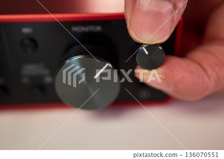 Adjusting audio controls, Precise handling of control knobs on audio equipment during setup, Fingers align control dials on audio interface for optimal sound calibration 136070551
