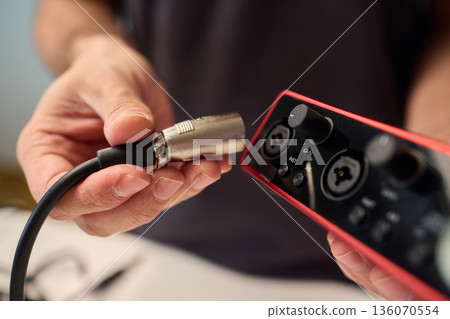 Preparation scene of connecting instrument cable to audio interface for recording, Detailed view of hand plugging instrument cable into red audio interface in studio setting Preparation scene of connecting instrument cable to audio interface for recording, Detailed view of hand plugging instrument cable into red audio interface in studio setting 136070554