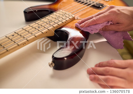 Closeup of guitar care and preparation process with studio lighting, Careful guitar body polishing and setup under professional studio lights before stage performance Closeup of guitar care and preparation process with studio lighting, Careful guitar body polishing and setup under professional studio lights before stage performance 136070578