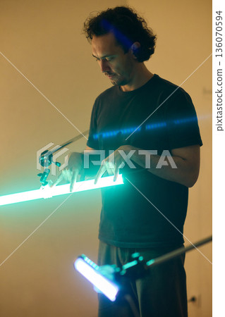 Professional adjusting illumination while managing studio supports meticulously, Creative technician balancing lights and equipment to achieve cinematic teal ambiance 136070594