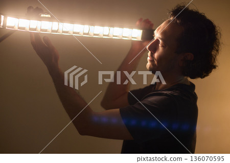 Professional adjusting illumination while managing studio supports meticulously, Creative technician balancing lights and equipment to achieve cinematic teal ambiance Professional adjusting illumination while managing studio supports meticulously, Creative technician balancing lights and equipment to achieve cinematic teal ambiance 136070595