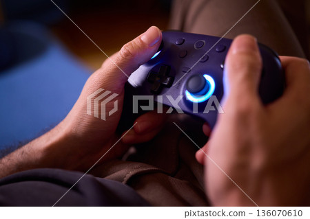 Comfortable man enjoying gameplay under colorful neon illumination, Chill indoor scene featuring smiling individual engaged in video game entertainment amid vivid purple lights 136070610