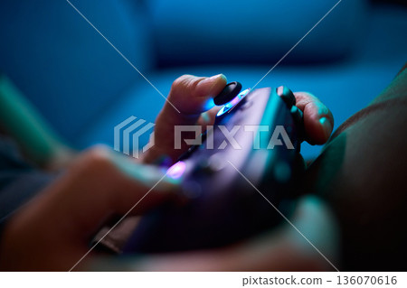 Comfortable man enjoying gameplay under colorful neon illumination, Chill indoor scene featuring smiling individual engaged in video game entertainment amid vivid purple lights 136070616