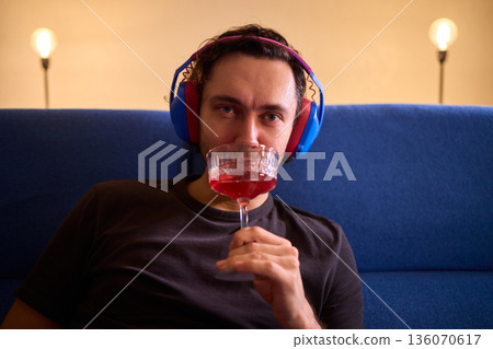 Relaxed man enjoying wine, Person wearing headphones rests peacefully, Creative professional enjoys evening relaxation with wine and soothing music in modern living space 136070617