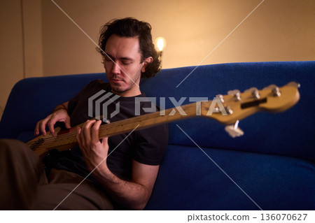Musician working in cozy studio, Casual musician practicing bass with effects and accents, Relaxed bassist intensely rehearsing in warmly lit home recording environment Musician working in cozy studio, Casual musician practicing bass with effects and accents, Relaxed bassist intensely rehearsing in warmly lit home recording environment 136070627