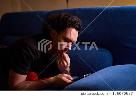 Chilled man on sofa, Casual individual reclining on sofa engrossed with mobile device, Unwinding man sits comfortably on sofa focused on his smartphone amid cozy modern decor Chilled man on sofa, Casual individual reclining on sofa engrossed with mobile device, Unwinding man sits comfortably on sofa focused on his smartphone amid cozy modern decor 136070657