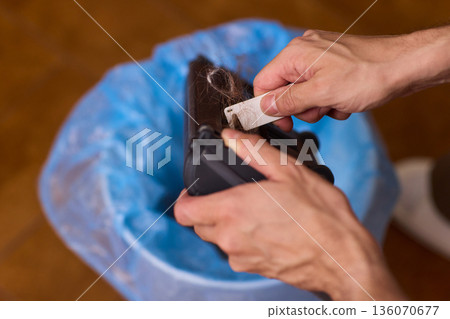 Vacuum filter cleaning. Closeup of vacuum filter being cleaned over trash bag background. Detail shot of cleaning vacuum filter with dust elimination and natural lighting 136070677