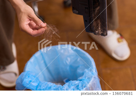 Vacuum filter cleaning. Closeup of vacuum filter being cleaned over trash bag background. Detail shot of cleaning vacuum filter with dust elimination and natural lighting 136070681