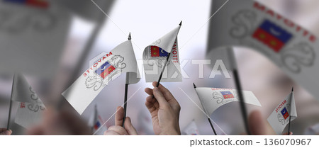 Mayotte flags in their hands on a blurred urban background 136070967