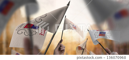 Mayotte flags in their hands on a blurred urban background 136070968