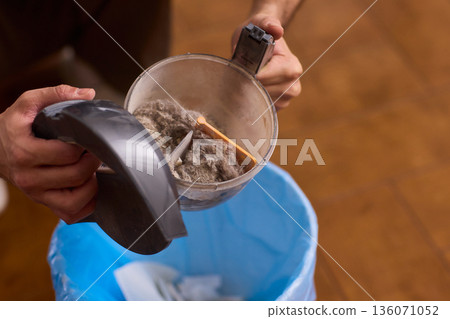 Practiced homeowner clearing clogged vacuum filter with visible dust particles. Closeup of homeowner performing routine vacuum cleaner filter cleaning with dust and hair visible 136071052