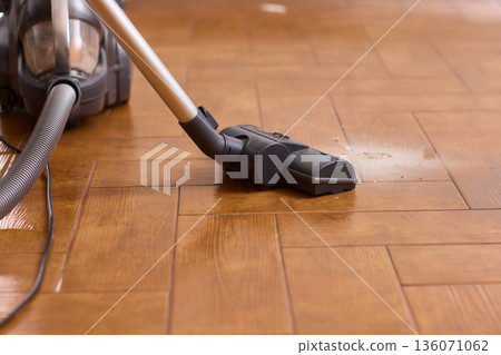 Hardwood floor vacuum head gliding across polished parquet, closeup of nozzle brushing wood grain, warm lighting, quiet household cleaning, gentle maintenance mood Hardwood floor vacuum head gliding across polished parquet, closeup of nozzle brushing wood grain, warm lighting, quiet household cleaning, gentle maintenance mood 136071062