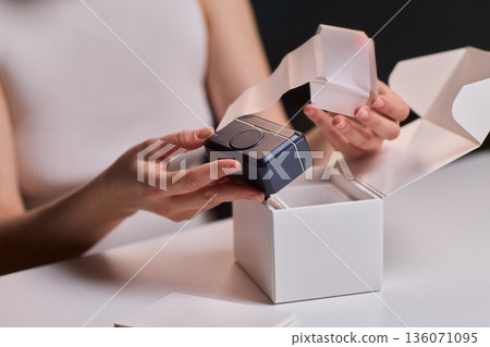 Closeup of hands opening clean packaging under controlled lighting. Lifestyle marketing shot emphasizing tactile clarity while revealing unbranded box in refined setting Closeup of hands opening clean packaging under controlled lighting. Lifestyle marketing shot emphasizing tactile clarity while revealing unbranded box in refined setting 136071095