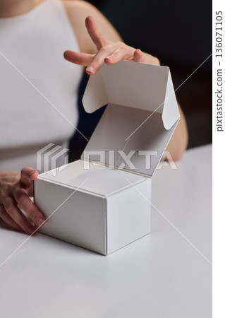 Closeup of hands opening clean packaging under controlled lighting. Lifestyle marketing shot emphasizing tactile clarity while revealing unbranded box in refined setting Closeup of hands opening clean packaging under controlled lighting. Lifestyle marketing shot emphasizing tactile clarity while revealing unbranded box in refined setting 136071105