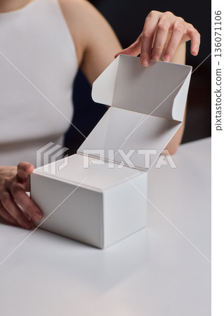 Closeup of hands opening clean packaging under controlled lighting. Lifestyle marketing shot emphasizing tactile clarity while revealing unbranded box in refined setting Closeup of hands opening clean packaging under controlled lighting. Lifestyle marketing shot emphasizing tactile clarity while revealing unbranded box in refined setting 136071106