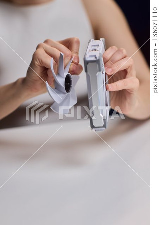 Detailed scene with technician disassembling small desktop fan carefully. Precise hands removing cover of desk fan during technical inspection with focused lighting 136071110