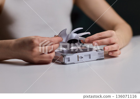 DIY fan repair. Hand fixing plastic fan blades. Closeup of assembling fan blades by hand. Engaging image of hands carefully attaching white blades onto motor hub for repair 136071116