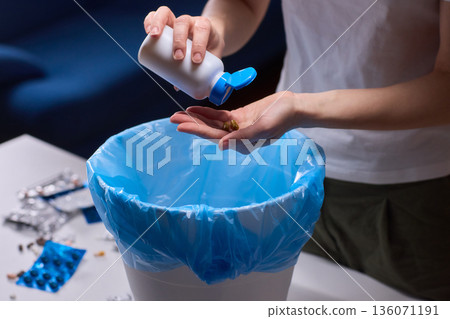 Responsible medication disposal in residential living space, An individual safely discards expired tablets from open containers into trash in living room setting Responsible medication disposal in residential living space, An individual safely discards expired tablets from open containers into trash in living room setting 136071191
