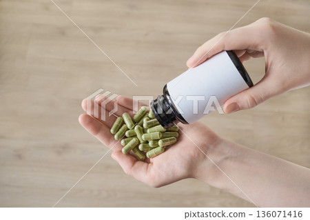 Women's hand dispensing green capsules from blank supplement bottle Women's hand dispensing green capsules from blank supplement bottle 136071416