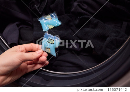Preparing laundry with ecofriendly capsule, Man placing detergent pod into frontload washer quickly, Homeowner readying machine for eco washing in modern laundry area Preparing laundry with ecofriendly capsule, Man placing detergent pod into frontload washer quickly, Homeowner readying machine for eco washing in modern laundry area 136071442