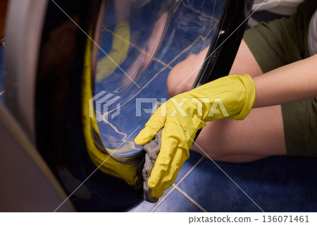 Washing glass door carefully now, Household cleaning of washing machine glass, Performing hygienic maintenance with circular motions on washing machine door glass 136071461