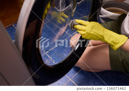 Washing glass door carefully now, Household cleaning of washing machine glass, Performing hygienic maintenance with circular motions on washing machine door glass Washing glass door carefully now, Household cleaning of washing machine glass, Performing hygienic maintenance with circular motions on washing machine door glass 136071462