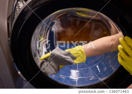 Washing glass door carefully now, Household cleaning of washing machine glass, Performing hygienic maintenance with circular motions on washing machine door glass 136071463