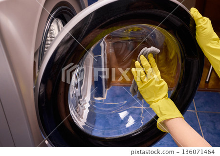 Washing glass door carefully now, Household cleaning of washing machine glass, Performing hygienic maintenance with circular motions on washing machine door glass Washing glass door carefully now, Household cleaning of washing machine glass, Performing hygienic maintenance with circular motions on washing machine door glass 136071464