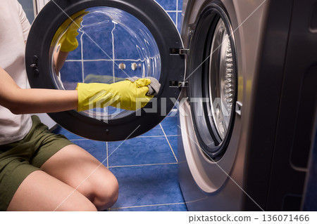 Washing glass door carefully now, Household cleaning of washing machine glass, Performing hygienic maintenance with circular motions on washing machine door glass Washing glass door carefully now, Household cleaning of washing machine glass, Performing hygienic maintenance with circular motions on washing machine door glass 136071466