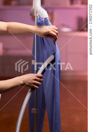 Blue shirt steaming, Blue uniform hanging while expertly steamed for wrinkle removal, Navy blue outfit on hanger being carefully steamed to remove creases professionally Blue shirt steaming, Blue uniform hanging while expertly steamed for wrinkle removal, Navy blue outfit on hanger being carefully steamed to remove creases professionally 136071502