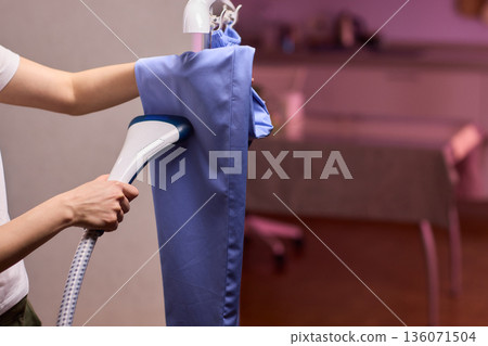Blue shirt steaming, Blue uniform hanging while expertly steamed for wrinkle removal, Navy blue outfit on hanger being carefully steamed to remove creases professionally Blue shirt steaming, Blue uniform hanging while expertly steamed for wrinkle removal, Navy blue outfit on hanger being carefully steamed to remove creases professionally 136071504