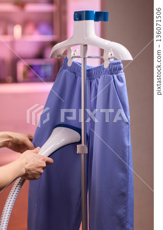Blue shirt steaming, Blue uniform hanging while expertly steamed for wrinkle removal, Navy blue outfit on hanger being carefully steamed to remove creases professionally 136071506