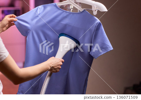 Blue shirt steaming, Blue uniform hanging while expertly steamed for wrinkle removal, Navy blue outfit on hanger being carefully steamed to remove creases professionally 136071509