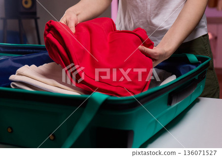 Organizing clothes before travel, Traveler arranges garments meticulously in their suitcase, An individual smoothly folds clothing and organizes suitcase for upcoming departure 136071527