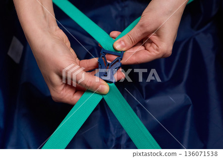 Hands tightening teal travel luggage strap, Closeup of hands attaching teal strap to luggage, Detailed shot of hands securing bright teal bag strap during travel preparation Hands tightening teal travel luggage strap, Closeup of hands attaching teal strap to luggage, Detailed shot of hands securing bright teal bag strap during travel preparation 136071538