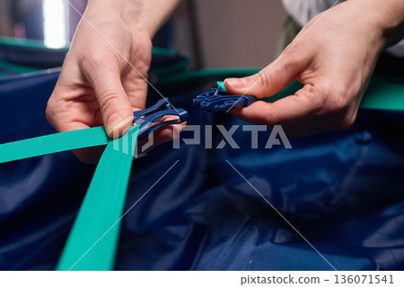 Hands tightening teal travel luggage strap, Closeup of hands attaching teal strap to luggage, Detailed shot of hands securing bright teal bag strap during travel preparation Hands tightening teal travel luggage strap, Closeup of hands attaching teal strap to luggage, Detailed shot of hands securing bright teal bag strap during travel preparation 136071541