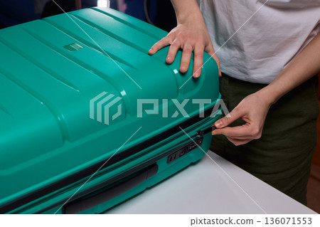 Traveler opening luggage, Close shot of hands unfastening suitcase zipper before travel, Detailed view of hands pulling zipper on vibrant teal travel case with anticipation Traveler opening luggage, Close shot of hands unfastening suitcase zipper before travel, Detailed view of hands pulling zipper on vibrant teal travel case with anticipation 136071553