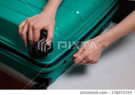 Traveler opening luggage, Close shot of hands unfastening suitcase zipper before travel, Detailed view of hands pulling zipper on vibrant teal travel case with anticipation Traveler opening luggage, Close shot of hands unfastening suitcase zipper before travel, Detailed view of hands pulling zipper on vibrant teal travel case with anticipation 136071554