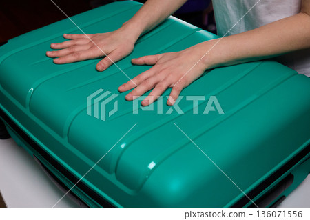 Traveler opening luggage, Close shot of hands unfastening suitcase zipper before travel, Detailed view of hands pulling zipper on vibrant teal travel case with anticipation Traveler opening luggage, Close shot of hands unfastening suitcase zipper before travel, Detailed view of hands pulling zipper on vibrant teal travel case with anticipation 136071556